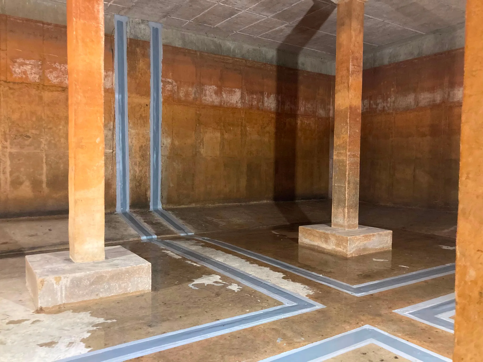 Interior of a potable water reservoir showing repaired joint sealant bands across the floor and columns