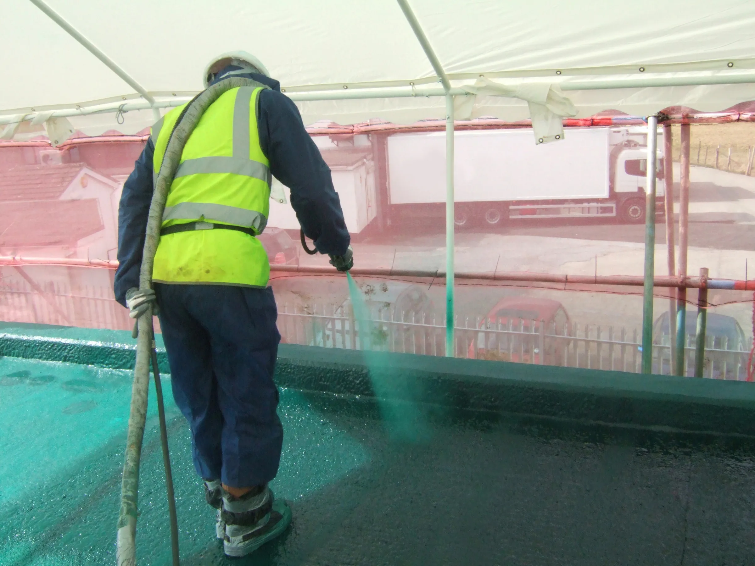 Two operatives spray-applying a pure polyurea waterproof membrane across a reservoir roof