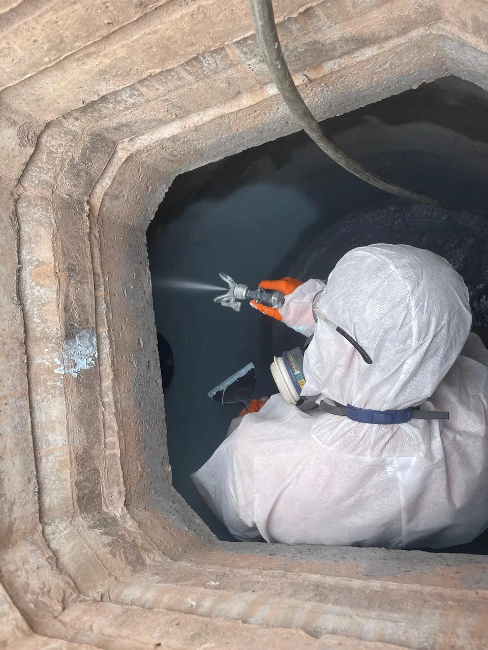 Operative spray-applying epoxy lining inside a brick manhole chamber at a waste handling facility